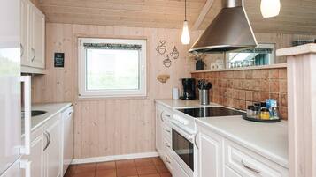 A kitchen with wooden walls, a window, a stove, and a sink.