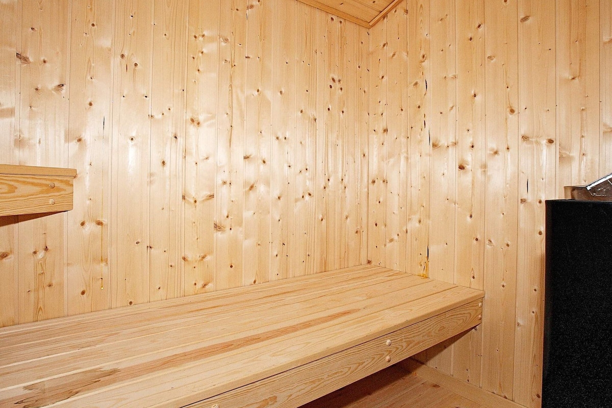 A wooden sauna room with a bench and a black heater.
