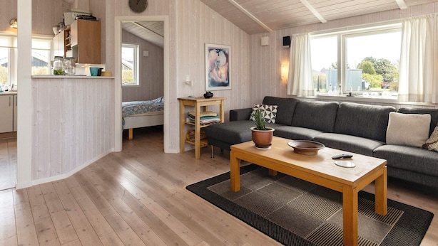 A modern living room with a wooden floor, a sofa, a coffee table, and a view of the outdoors through large windows. - 5 Star Holiday Home in Hadsund (Hadsund)