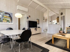 A modern living room with a dining area, a flat-screen TV, and a kitchen in the background.