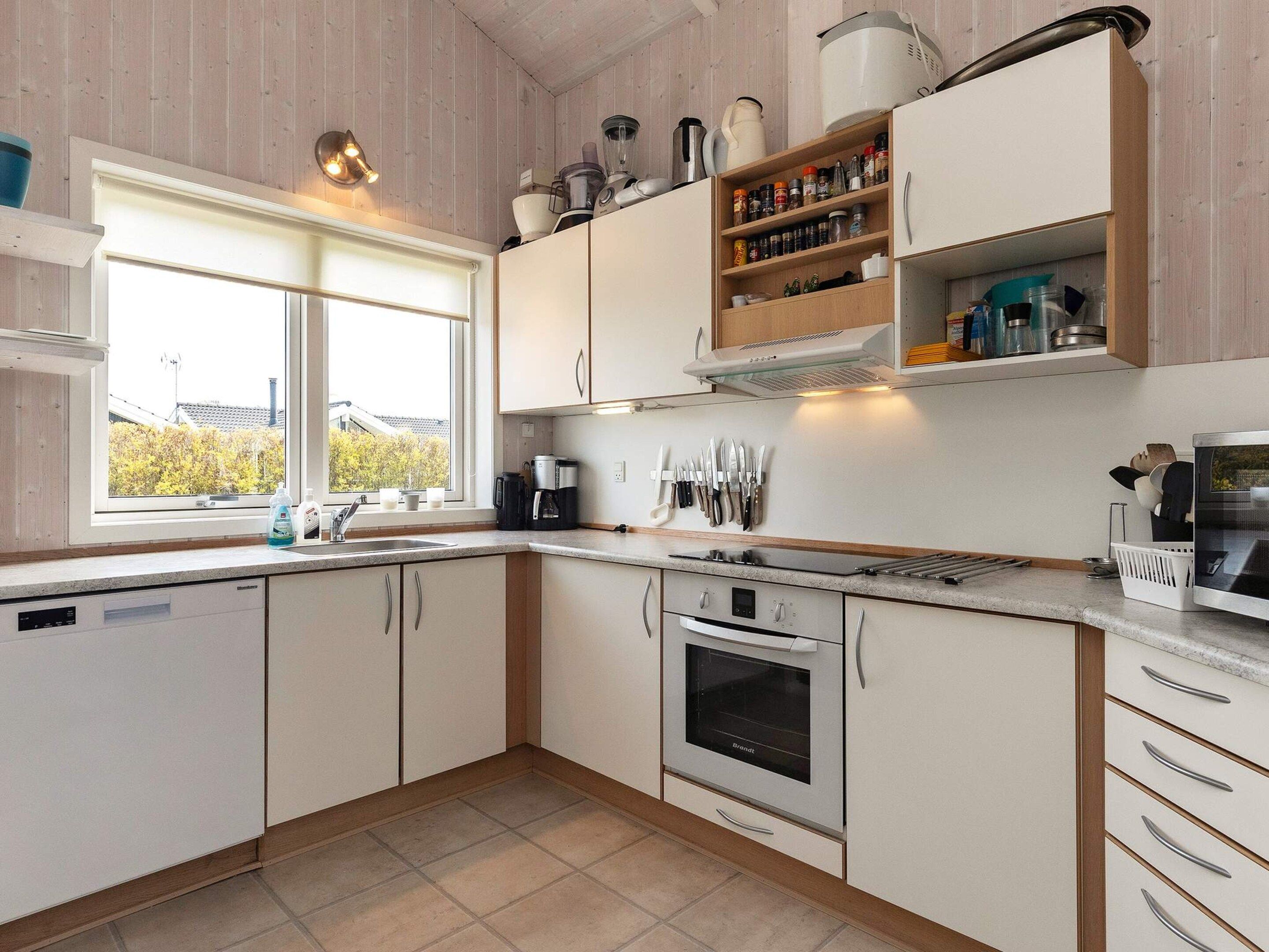A kitchen with white cabinets, a built-in oven, a coffee maker, and a window with a view of trees.