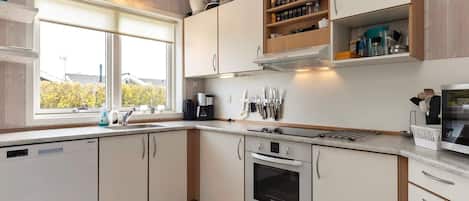 A kitchen with white cabinets, a built-in oven, a coffee maker, and a window with a view of trees.