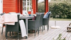 A deck with wicker furniture and a table, a red building in the background, and a clear sky. - 4 Star Holiday Home in Vinderup (Vinderup)