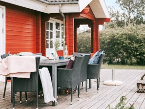 Une terrasse dotée de meubles en osier et d’une table, un bâtiment rouge en arrière-plan et un ciel dégagé.