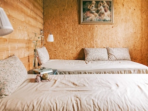 Camera da letto con parete in legno, un letto con biancheria a fiori, un comodino con libri e un quadro sopra il letto.