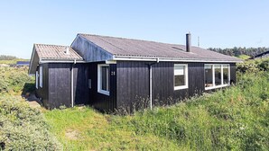 Ein eingeschossiges Holzhaus mit dunkler Fassade, einem Schornstein und einer kleinen Veranda.