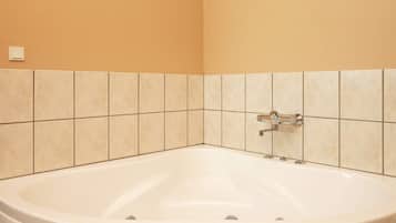 Un baño con bañera, paredes con azulejos e interruptor de luz a la vista.