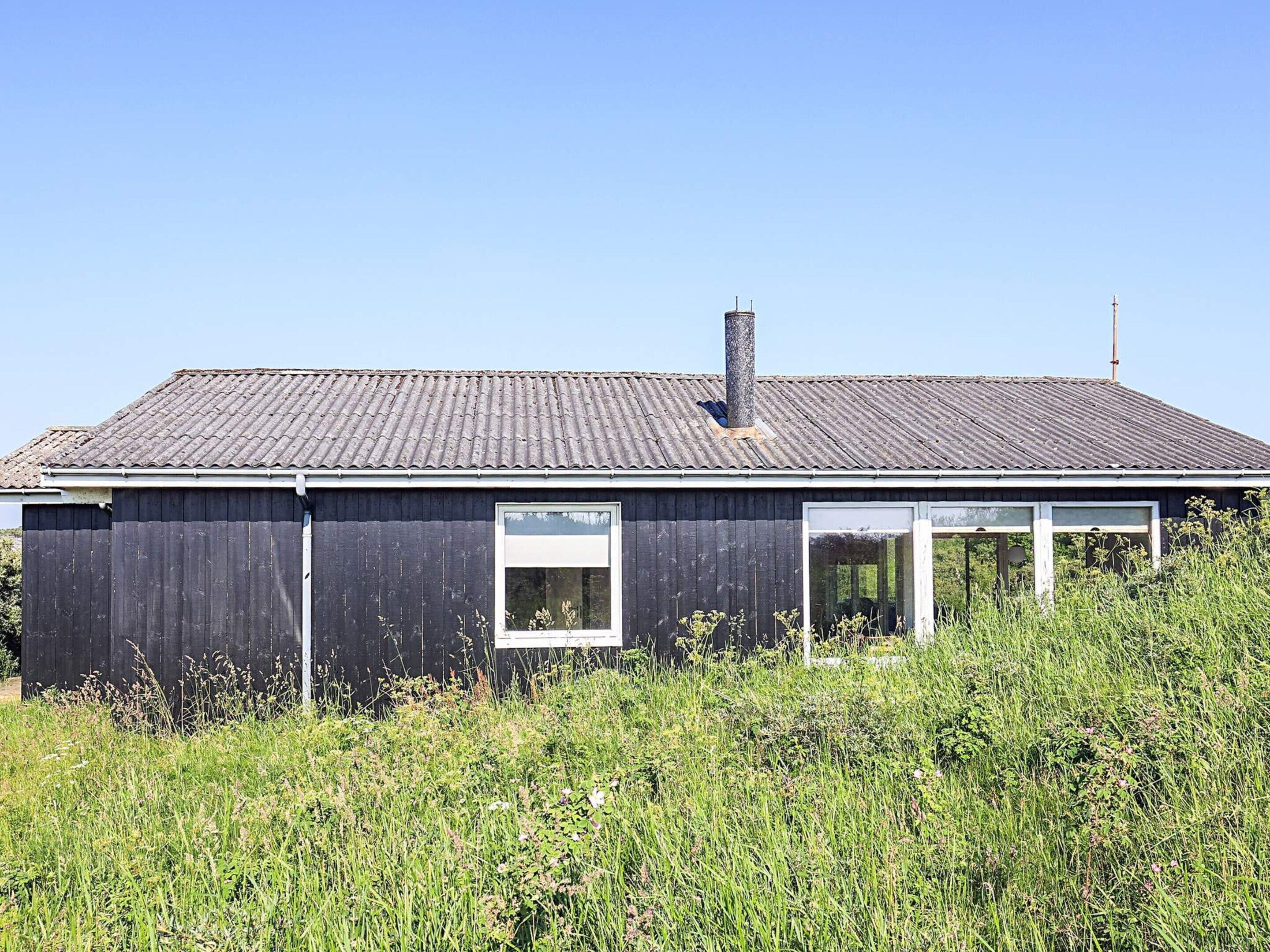 A single-story building with a dark exterior, a metal roof, and a chimney.