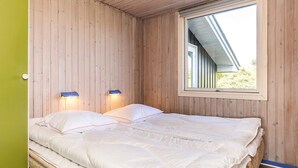 Ein Zimmer mit einem Bett, Holzwänden, einem Fenster und zwei Wandleuchten.