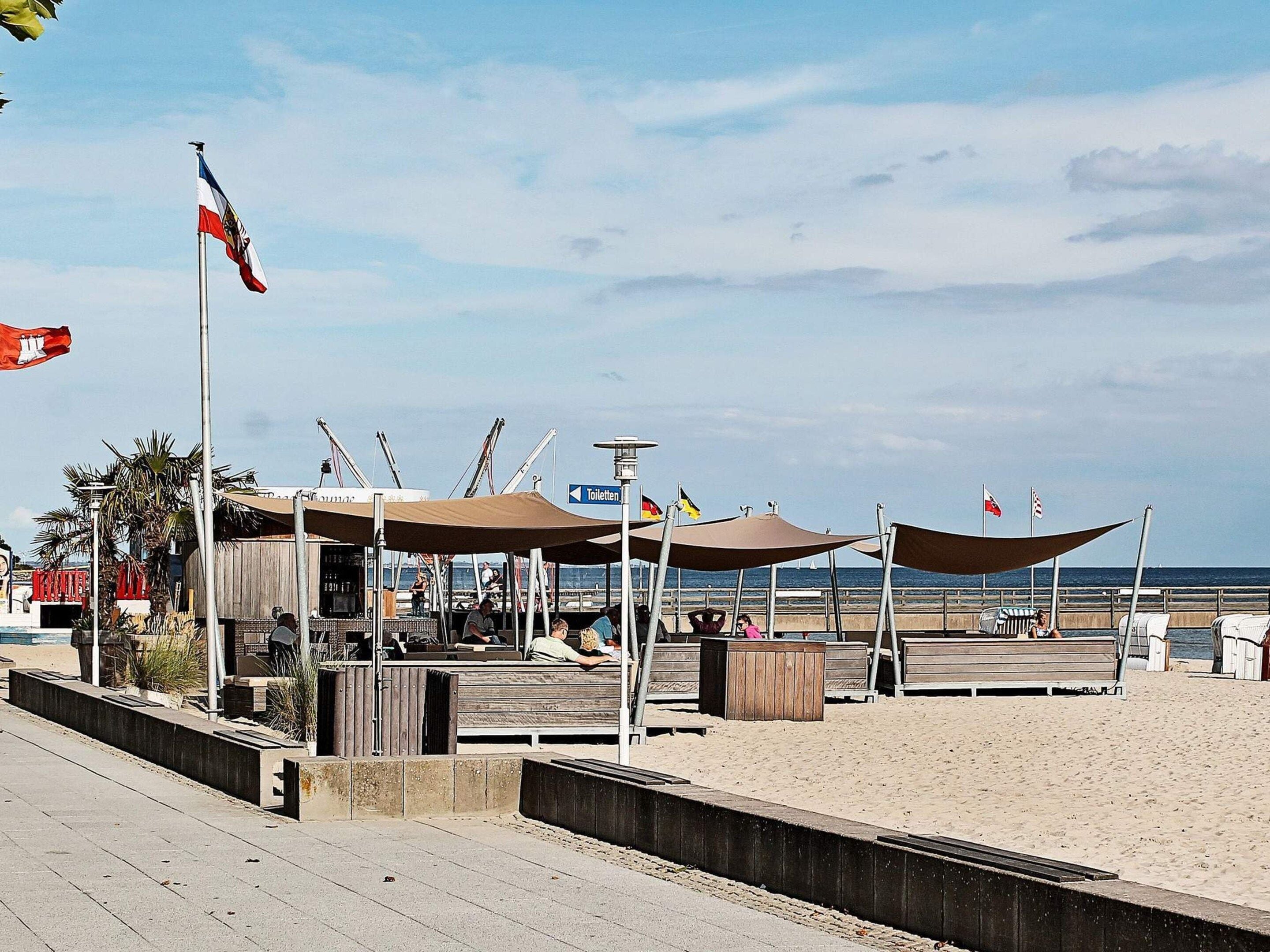 A beachside promenade with a wooden walkway, shaded seating areas, and a view of the sea.