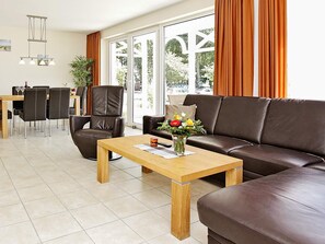 Uma sala de estar moderna com sofá, cadeiras, uma mesa de centro e um espaço de jantar com mesa e cadeiras.