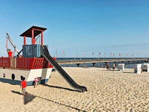 Una playa con una torre de salvavidas, un tobogán y un muelle que se adentra en el agua.