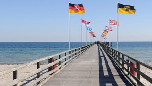 Une jetée avec une promenade en bois menant à la mer, bordée de drapeaux de différents pays.