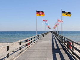 Un muelle con un paseo de madera que conduce al mar, flanqueado por banderas de varios países.