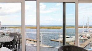 Une vue depuis un balcon doté d’une terrasse en bois, donnant sur une marina avec des bateaux et une côte lointaine.