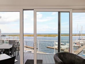 Une vue depuis un balcon doté d’une terrasse en bois, donnant sur une marina avec des bateaux et une côte lointaine.