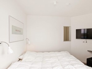 A minimalist bedroom with a bed, a mounted TV, and a framed picture on the wall.