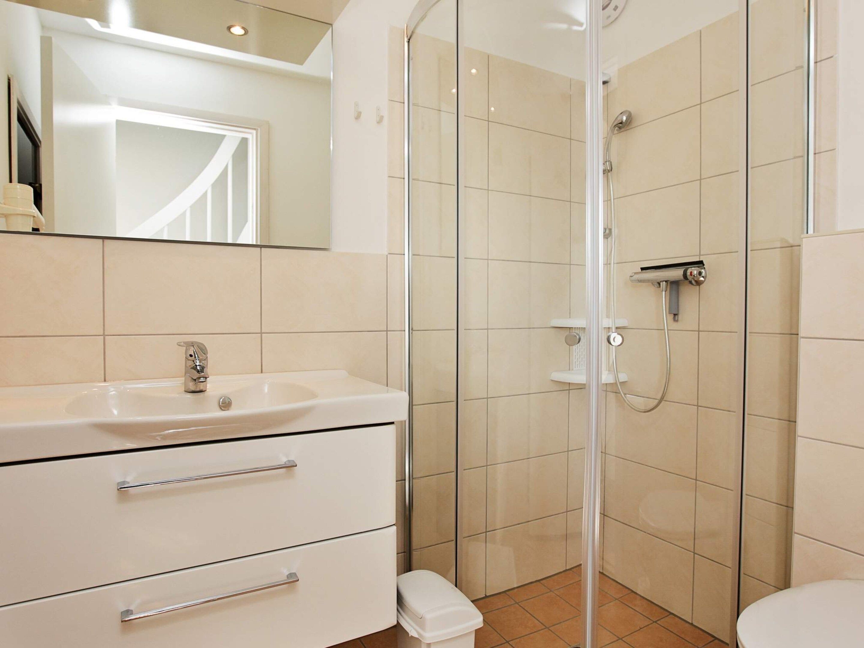 A bathroom with a white sink, a mirror, a shower enclosure, and a toilet.