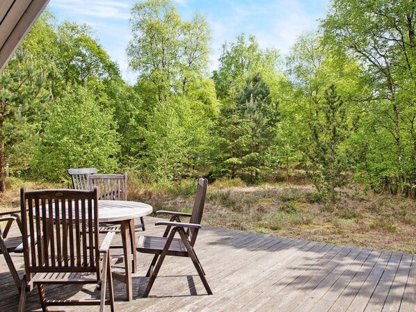 An outdoor patio with a wooden deck, a round table, and two wooden chairs.