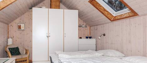 A bedroom with a lofted ceiling, a bed, a wardrobe, a chair, and a small table.