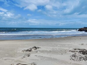 A beach with waves, a clear sky, and rocky outcrops.