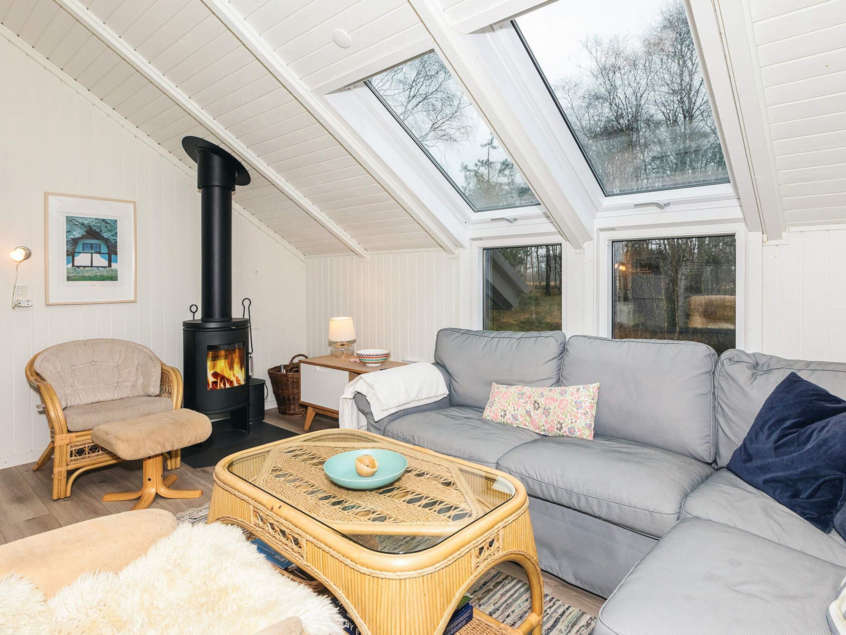 A cozy living room with a sofa, a chair, a table, a fireplace, and skylights.