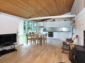 Una cocina moderna con armarios blancos, una zona de comedor con sillas de madera, un televisor y una chimenea.