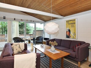 A modern living room with a wooden ceiling, a large window, a sofa, a table, and a poster on the wall. - 6 Person Holiday Home in Saltum (Saltum)
