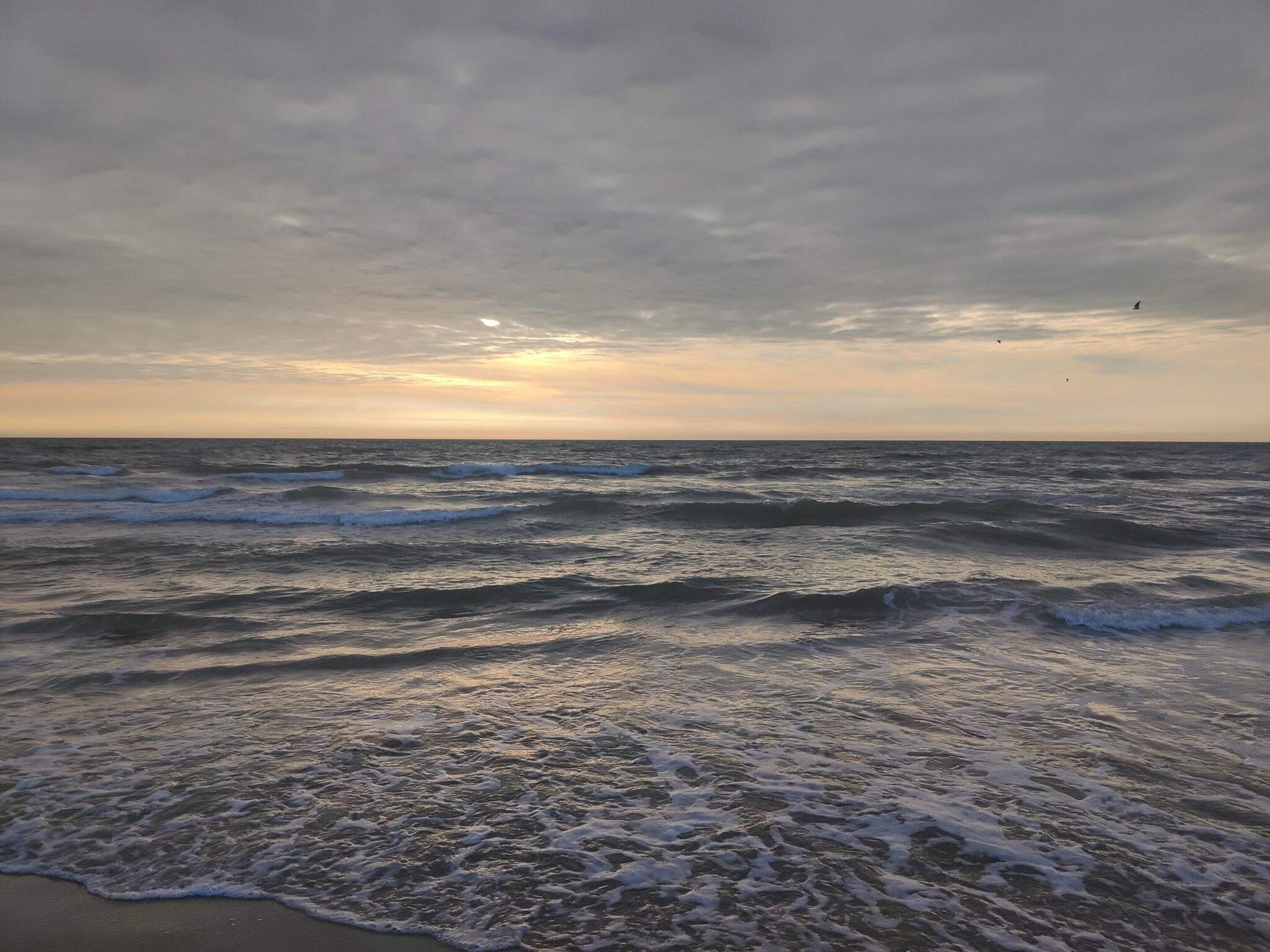 Una playa con olas y cielo nublado.