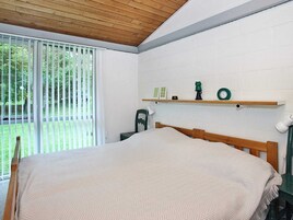 Un dormitorio con una cama, una ventana con persianas, techo de madera y un estante con un reloj y un objeto verde.
