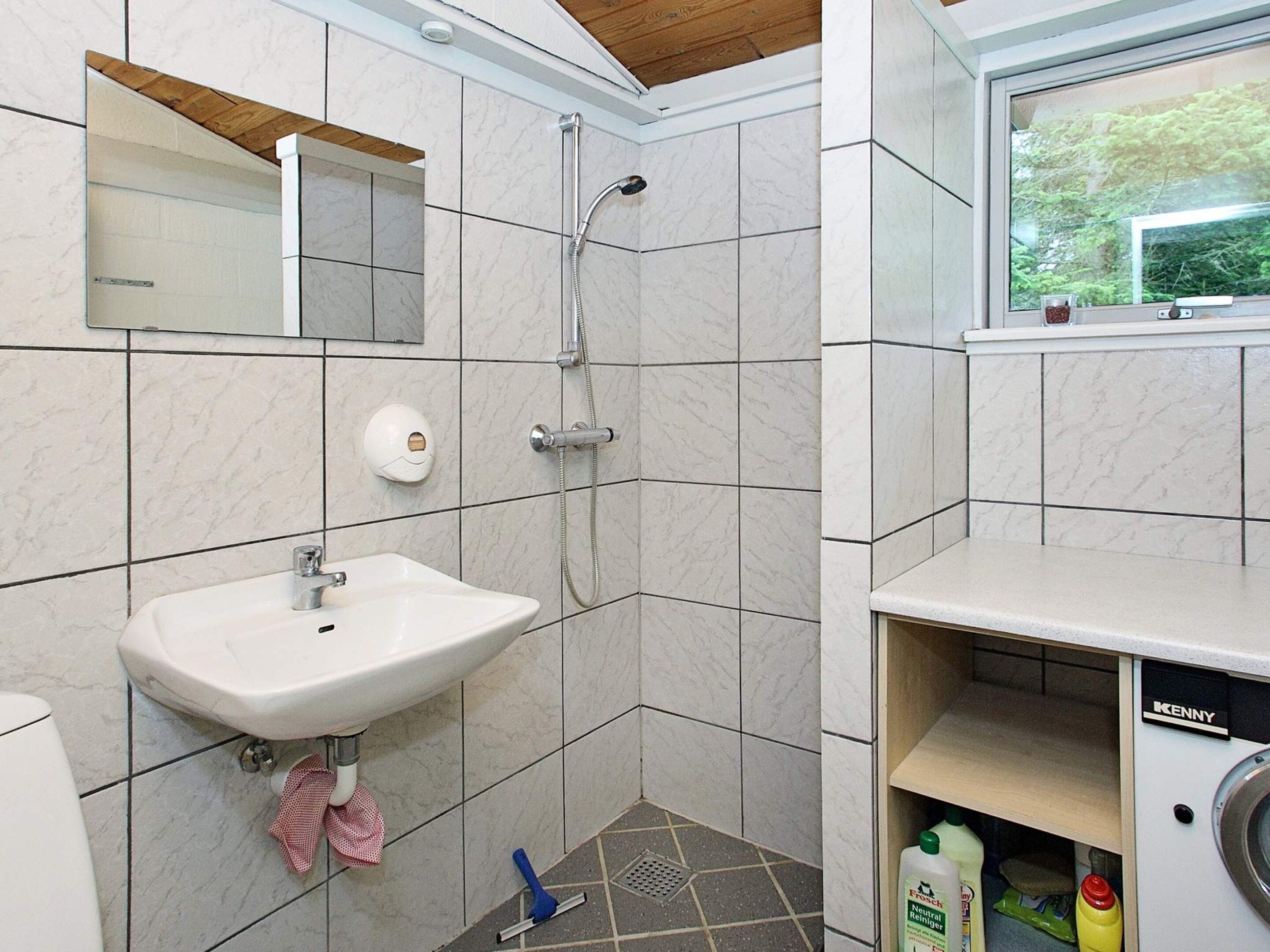 A bathroom with a sink, mirror, shower, and a window with a view.