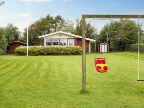 A well-maintained lawn with a swing set and a house with a red exterior and white trim. - 8 Person Holiday Home in Struer (Struer)