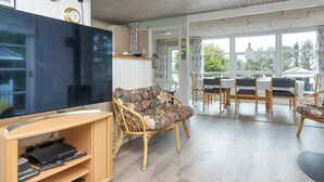 Un salon comprenant un téléviseur, un canapé, une table à manger avec des chaises et une grande fenêtre.