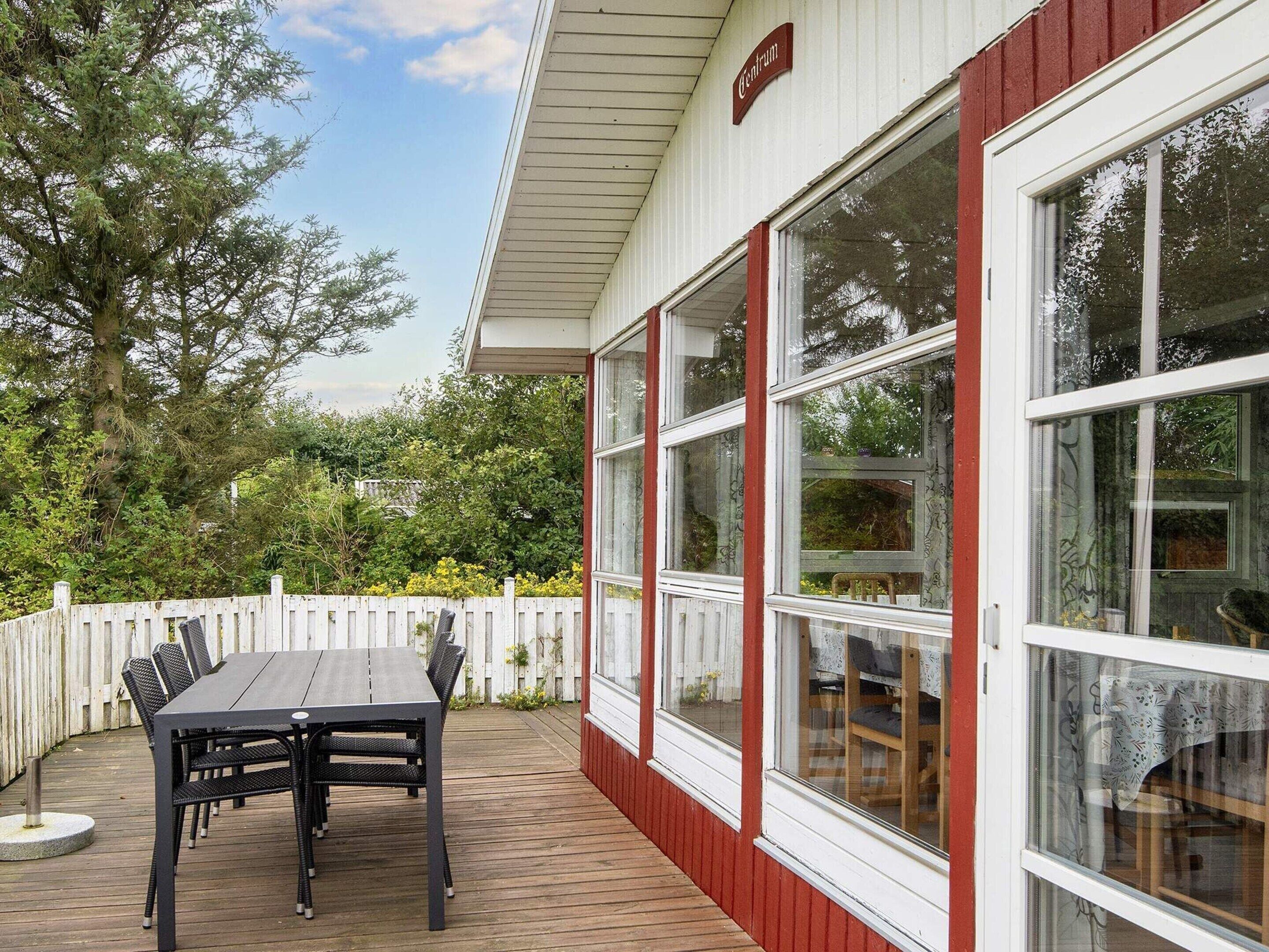 A covered patio with a table and chairs, a white fence, and large windows.
