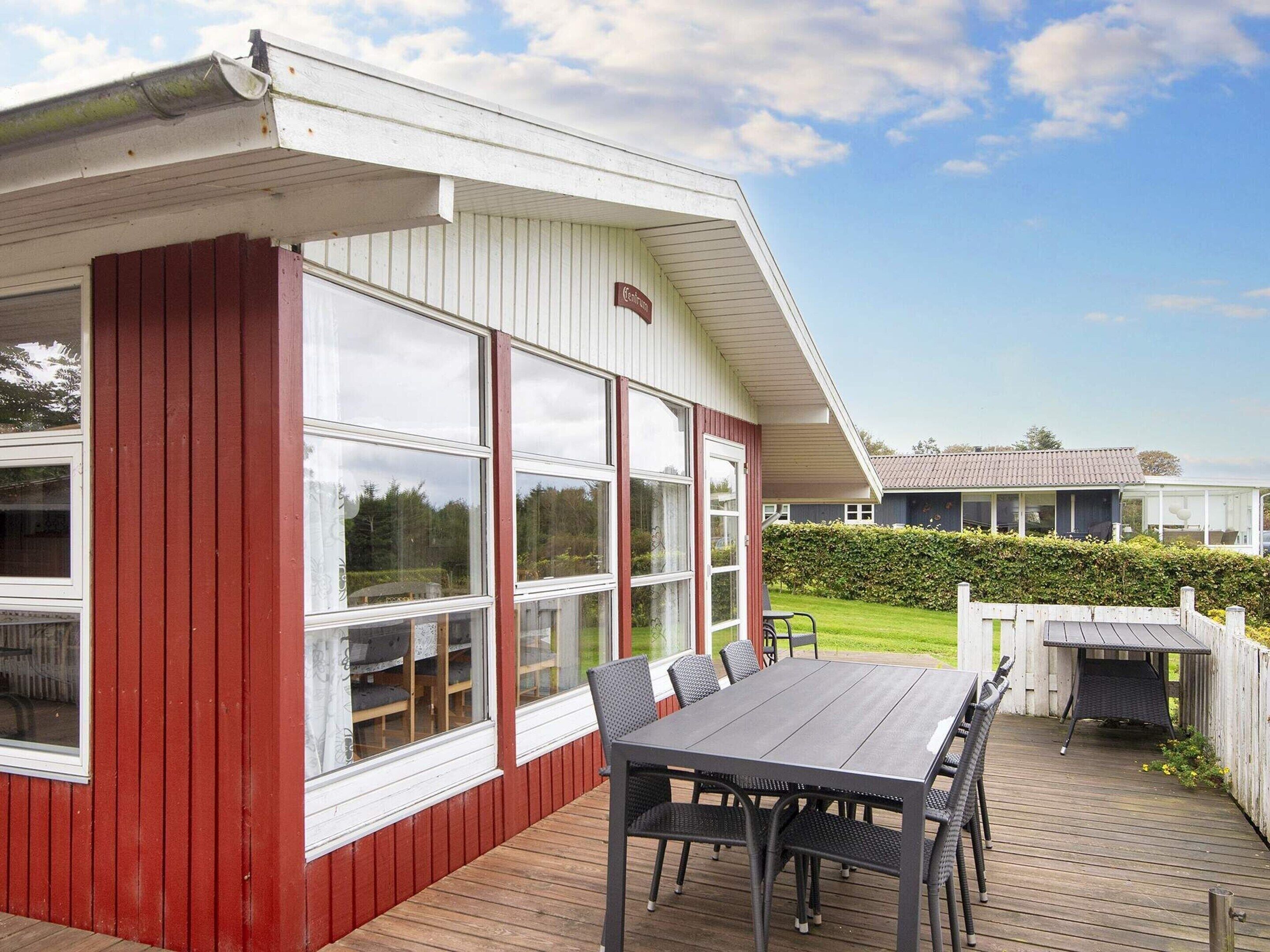 A covered outdoor area with a table and chairs, large windows, and a view of a house in the background.