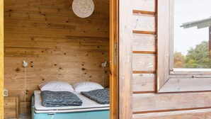 Une pièce de cabane en bois comprenant un lit, un luminaire suspendu et une fenêtre.