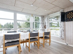 A dining area with a table and chairs, large windows, and a dartboard on the wall.
