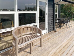 A wooden deck with a bench, a table with chairs, and a sliding glass door leading to a patio area.