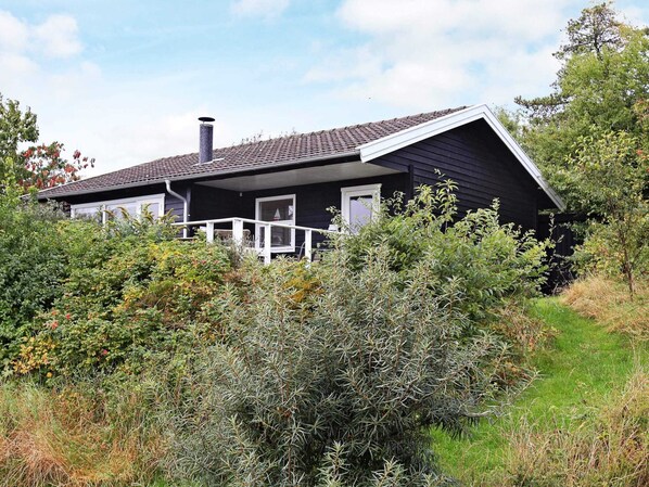 A house with a sloped roof, a chimney, and a porch with a railing.