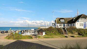 A coastal hotel with a thatched roof, a small adjacent structure, and a view of the sea.