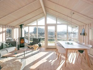 Una habitación amplia con techo alto, ventanas grandes, chimenea, zona de comedor y un rincón de estar acogedor.