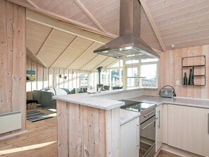 A modern kitchen with a central island, wooden walls, and a large window providing a view. - 5 Star Holiday Home in Thisted (Thisted)