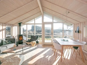 A spacious room with a high ceiling, large windows, a fireplace, a dining table with chairs, and a sofa. - 5 Star Holiday Home in Thisted (Thisted)