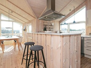 A modern kitchen with wooden paneling, a central island with stools, and large windows providing natural light.