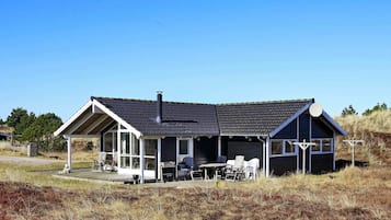 A single-story building with a dark roof and white trim, featuring a covered outdoor seating area with tables and chairs.