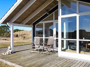 A covered outdoor seating area with two wooden chairs and a table, overlooking a grassy landscape. - 5 Star Holiday Home in Thisted (Thisted)