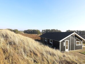 A single-story building with a dark roof and white trim, situated on a grassy hill with a clear sky. - 5 Star Holiday Home in Thisted (Thisted)