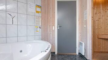 Un baño con una bañera blanca, una puerta de madera y paredes con azulejos.