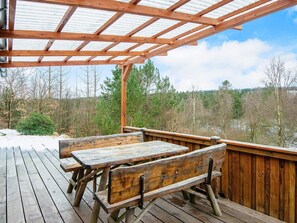 Une terrasse en bois, dotée de tables de pique-nique et de bancs, qui offre une vue sur une zone boisée.