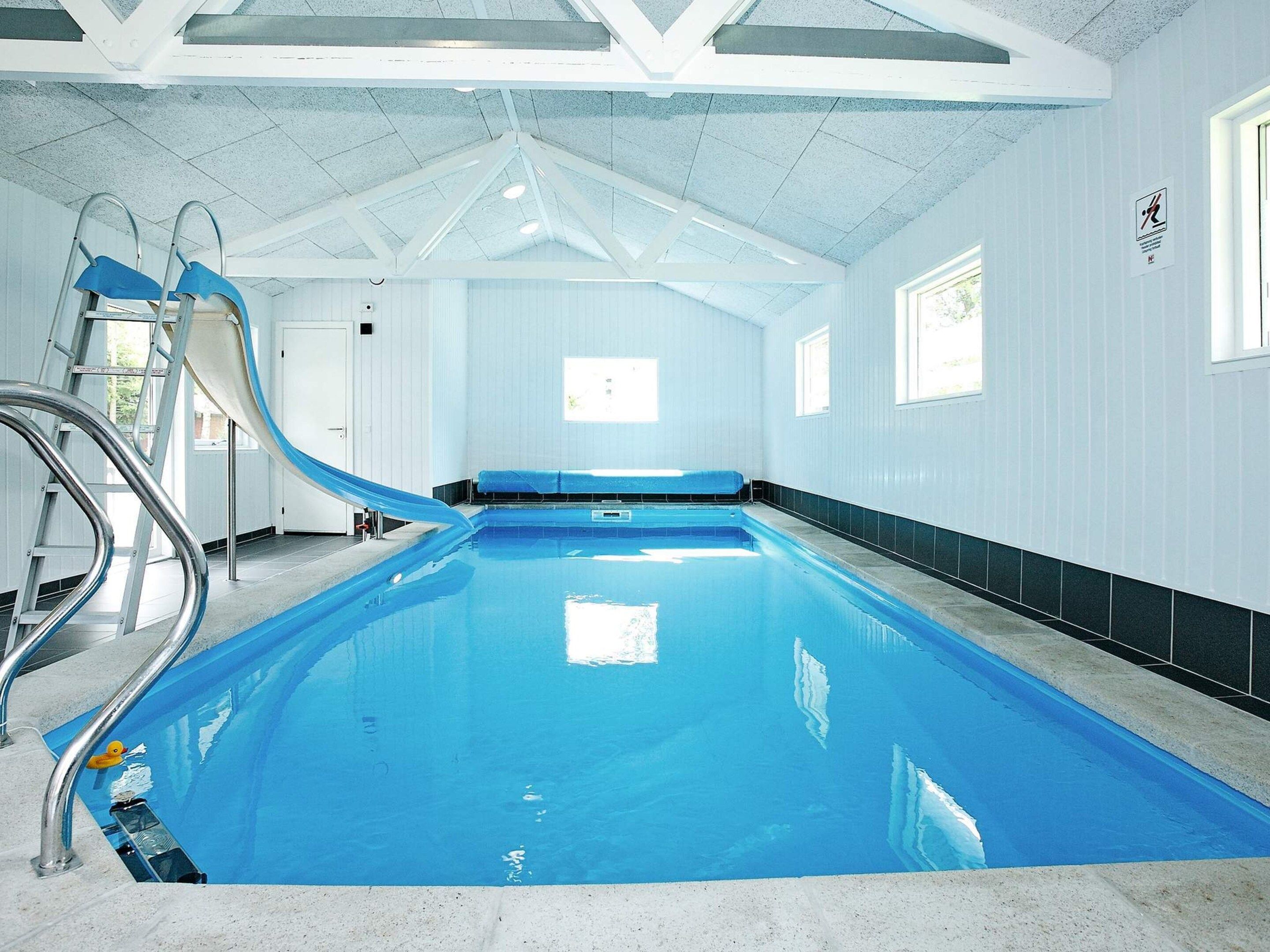 Une piscine intérieure avec un toboggan, une échelle et une fenêtre.